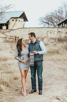 a man and woman standing next to each other on a dirt road in front of a barn