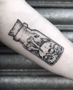 a man's arm with a bottle filled with skulls and bones on the inside