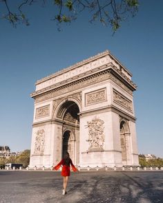 a woman in a red dress is walking towards the arc de trioe triumph monument