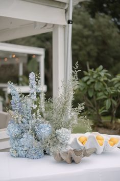 an egg carton sitting on top of a table next to blue flowers and greenery