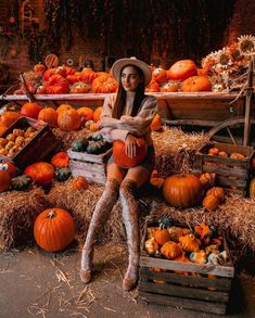 a woman sitting on top of a pile of hay next to lots of pumpkins