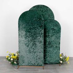 two green sculptures sitting on top of a wooden floor next to yellow flowers and greenery