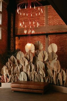 an arrangement of paper flowers in front of a brick wall with chandelier hanging from the ceiling