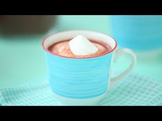 a blue mug filled with hot chocolate and marshmallows sitting on top of a table