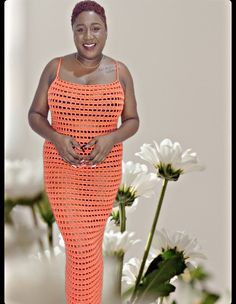 a woman in an orange crochet dress standing next to white flowers and smiling