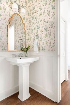 a white pedestal sink sitting under a mirror in a bathroom next to a wallpapered wall