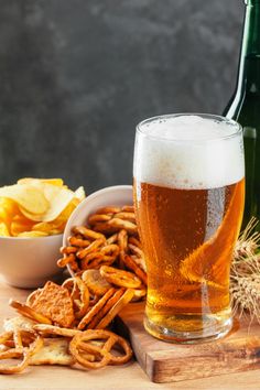 a glass of beer next to some pretzels and chips