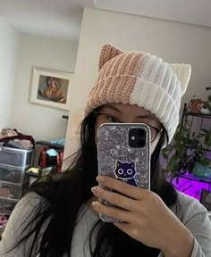 a woman taking a selfie with her phone in front of her face and wearing a cat hat