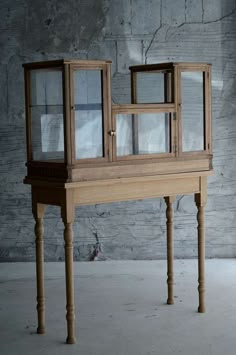 a small wooden table with glass windows on it's top and bottom shelf, in front of a brick wall