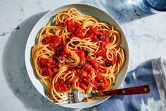 a plate of spaghetti with tomato sauce and a fork on a marble counter top next to a bottle of water