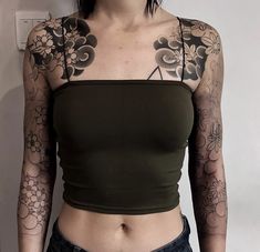 a woman with tattoos on her arms and chest is standing in front of a wall