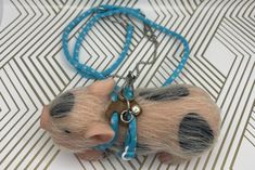 a small toy pig is on a blue cord with a keychain around it's neck