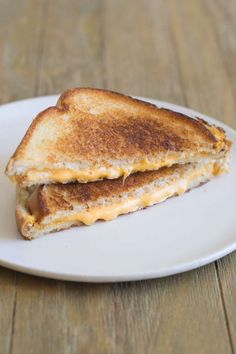 a grilled cheese sandwich on a white plate sitting on a wooden table with a fork