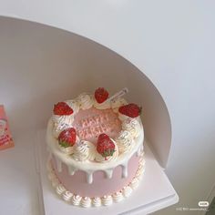 a pink cake with white frosting and strawberries on top sitting on a table