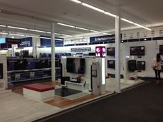 an entertainment center with several televisions on the wall and people walking around in the background