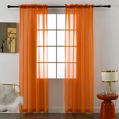 an orange sheer curtain hangs in front of a white wall with a chair and lamp