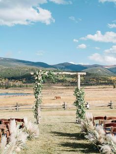 an outdoor ceremony setup with chairs and flowers on the grass, in front of mountains