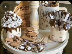 some cookies and marshmallows are on a tray next to mugs with hot chocolate