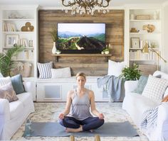 a woman is sitting in the middle of a living room doing yoga