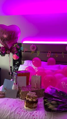 a bed topped with lots of pink balloons next to a table filled with food and gifts