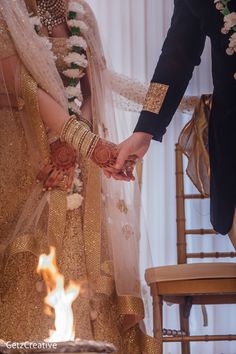 a bride and groom holding hands in front of a fire