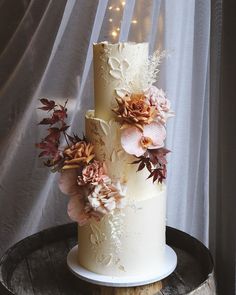 a three tiered wedding cake with flowers on the top and bottom is sitting on a wooden barrel