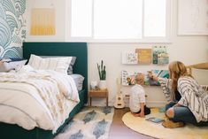 a woman sitting on the floor in front of a bed with a baby next to it