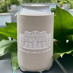 a can cooler sitting on top of a table next to some green leafy plants