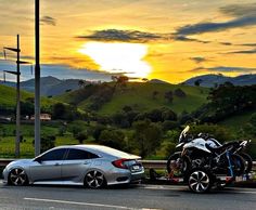 a motorcycle on the back of a car being towed by a tow truck in front of a green hillside