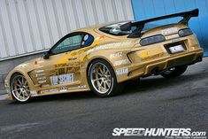 a gold sports car parked in front of a building with graffiti on it's side