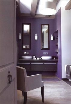 a bathroom with purple walls and two sinks in the center, along with a white chair