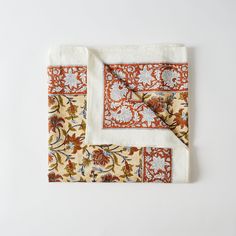 an orange and white floral print pocket square on a white tablecloth with two matching napkins