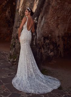 a woman standing in front of a rock wall wearing a wedding dress with an open back