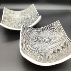 two silver plates sitting on top of a black table next to each other with designs on them