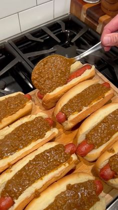 several hotdogs with chili on them sitting on top of a wooden cutting board