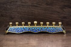 a blue and gold candle holder with five candles on the top, in front of a wooden background