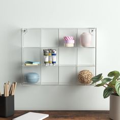 a white shelf filled with lots of different items on top of a wooden table next to a potted plant