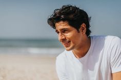 a man sitting on top of a sandy beach next to the ocean with his eyes closed