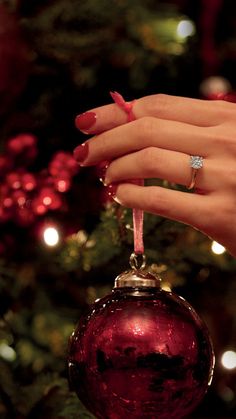 a woman's hand holding a christmas ornament with a diamond ring on it