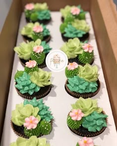 cupcakes decorated with green and pink flowers are in a box on the table