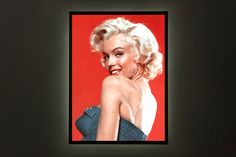 a marilyn monroe photo hanging on a wall in front of a red background with black frame