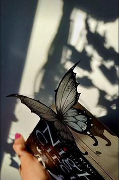 a person holding up a book with a butterfly on it's cover and the shadow of a tree in the background