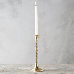 a gold candle holder with a single white candle in it's center on a wooden table