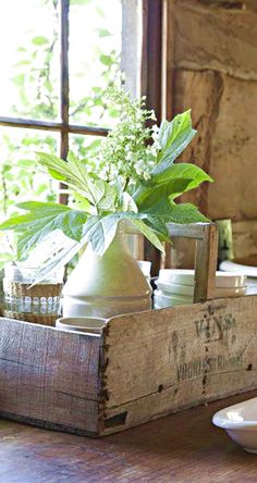 a wooden box with some plants in it on a table next to plates and cups