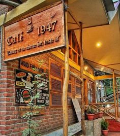 the outside of a restaurant with wooden signs on it's walls and plants in pots