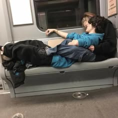 two people are sleeping on a subway train bench with their arms wrapped around each other