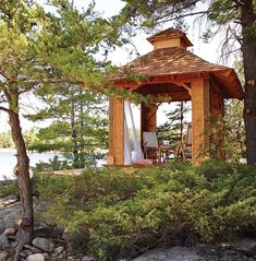 a wooden gazebo sitting on top of a lush green forest next to a lake