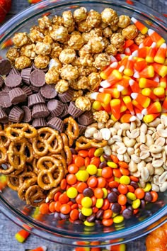 a glass bowl filled with candy corn, pretzels, and halloween treats