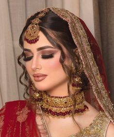 a woman in a red and gold bridal outfit with jewelry on her head, looking to the side