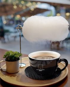 a cup of coffee sitting on top of a wooden table next to a potted plant